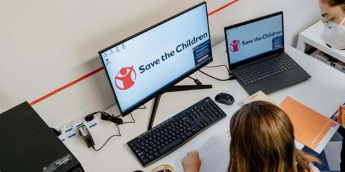 Bambina e volontaria al pc con scritta Save the Children sullo schermo