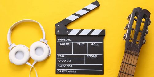 Cuffie musicali, ciak e manico chitarra su fondo giallo