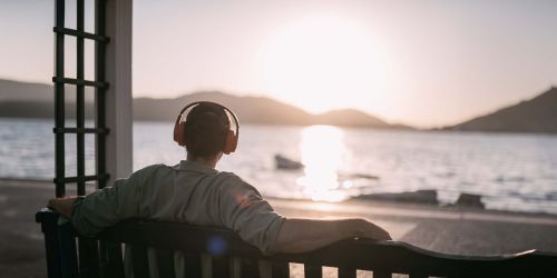 Ragazzo di spalle ascolta la musica seduto su una panchina guardando il lago