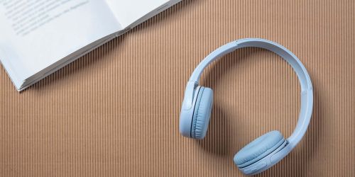 Cuffie per ascoltare musica appoggiate su un piano. In alto a sinistra angolo di un libro