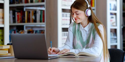 Studentessa con cuffie per ascoltare musica che studia in biblioteca