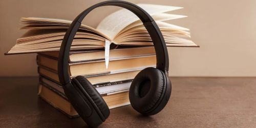 Cuffie musicali appoggiate a pila di libri. In cima libro aperto