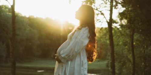 Donna in gravidanza nel verde di un parco con sole che la illumina