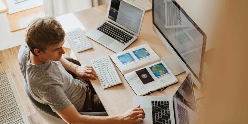 Giovane uomo seduto alla scrivania con due pc portatili grande schermo e appunti