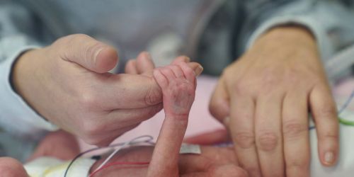 Mamma che tiene la mano di neonato prematuro in una incubatrice