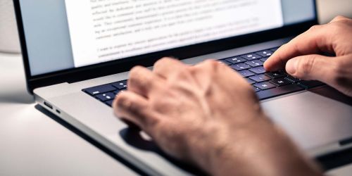 Dettaglio di mani che scrivono al computer portatile, sullo schermo foglio di testo