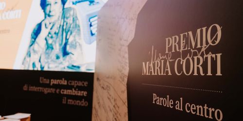 Foto scattata durante la premiazione della 1ª edizione del Premio: in primo piano un pannello con il nome del Premio, sullo sfondo slide con fotografia di Maria Corti