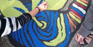 Mani con pennelli che dipingono il logo di Moruzzi Road sulla strada