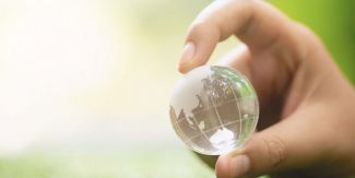 Mano che tiene tra l'indice e il pollice un modellino in vetro della Terra