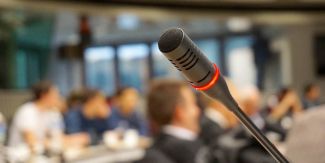 Microfono in primo piano. Sulla sfondo, sfuocati, i partecipanti a un meeting