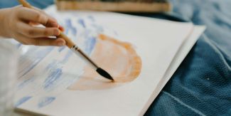 Mano di bambino tiene in mano pennello mentre dipinge su un foglio