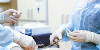 Due medici intenti a mettere dei punti a paziente sdraiato su lettino