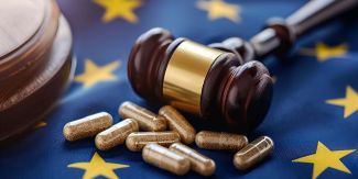 Capsule di farmaci appoggiate su bandiera dell'Europa su cui poggia anche martelletto da giudice