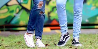 Gambe di due giovani che indossano jeans e scarpe da ginnastica, sullo sfondo dei murales