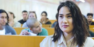 Studentessa internazionale in primo piano seduta in un aula UniPv. Dietro di lei altri studenti e studentesse