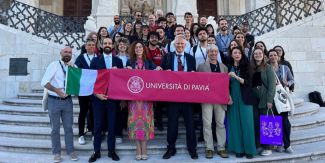 Foto di gruppo del team dell'Università di Pavia presente all'EC2U Forum di Coimbra su una scalinata. I presenti nella prima fila reggono striscione con il logo UniPv
