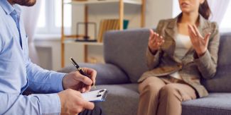 A sinistra psicologo seduto con appunti, di fronte a lui donna che parla su un divano