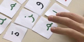 Foglietti con simboli dell'alfabeto arabo e dita delle mani di un bambino che li combina per formare delle parole