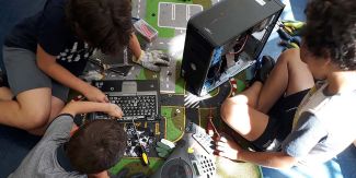 Bambini, fotografati dall'alto, mentre svolgono il laboratorio "Smonting" con delle componenti di computer