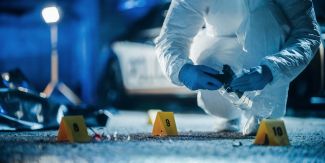 Scena del crimine con numeri segna reperti e operatore che effettua rilievi