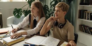 Ragazza e ragazzo adolescenti seduti a una scrivania su cui sono presenti libri e penne