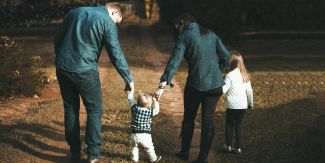 Famiglia: papà e mamma che tengono per mano bambino piccolo e bambina, di spalle