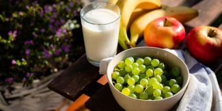 Tavola con uva, mele, banane e un bicchiere di latte