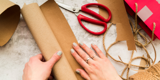 Mani femminili che maneggiano carta da pacchi, spago e forbici