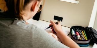 Ragazzina di spalle seduta alla scrivania mentre fa i compiti