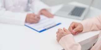 Dettaglio su scrivania a cui siedono paziente e medico che scrive su una cartelletta