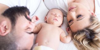 Neonato sdraiato in mezzo ai genitori