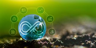 Immagine rappresentativa dell'economia circolare: campo su cui è posato globo terrestre circondato da simboli legati a sostenibilità, energia, ambiente