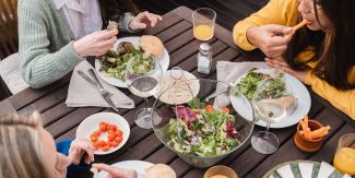 Tre ragazze sedute a un tavolo che mangiano cibo sano: verdure, pane, ecc.