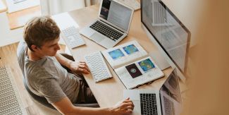 Giovane uomo seduto alla scrivania con due pc portatili grande schermo e appunti