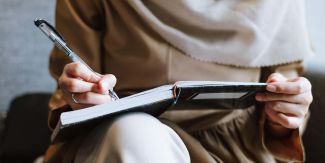 Dettaglio su mano di donna seduta che scrive su un quaderno appoggiato al ginocchio