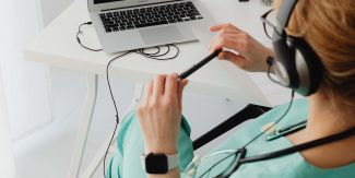 Dottoressa con stetoscopio al collo e cuffie seduta davanti a un pc portatile