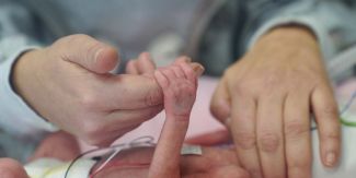 Mamma che tiene la mano di neonato prematuro in una incubatrice