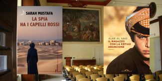 Copertine dei libri "La spia ha i capelli rossi" e "Il ragazzo con la kefiah arancione", sullo sfondo l'Aula Magna del Collegio F.lli Cairoli