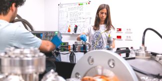 Una ricercatrice che indossa la maglietta con il logo UniPv e un ricercatore di spalle in uno dei laboratori dell'Università di Pavia