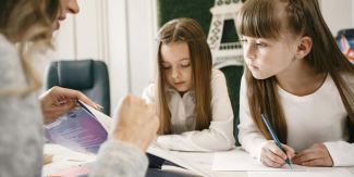 Bambine che fanno i compiti con una persona adulta che le aiuta