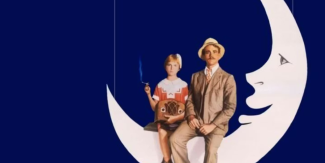 I due protagonisti del film "Luna di carta" seduti sulla sagoma di una luna di cartone