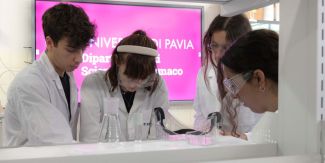 Tre ricercatrici e un ricercatore in uno dei laboratori del Dipartimento di Scienze del Farmaco UniPv. Sullo sfondo uno schermo con il logo del Dipartimento.