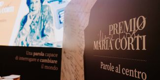 Foto scattata durante la premiazione della 1ª edizione del Premio: in primo piano un pannello con il nome del Premio, sullo sfondo slide con fotografia di Maria Corti