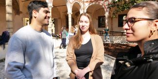 Due studentesse e uno studente in uno dei cortili UniPv. Sullo sfondo più sfuocati altri studenti
