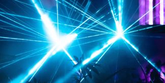 Spettacolo di luci laser proiettato in un ambiente scuro, con effetti luminosi che creano fasci e riflessi geometrici tra vegetazione o elementi d'arredo